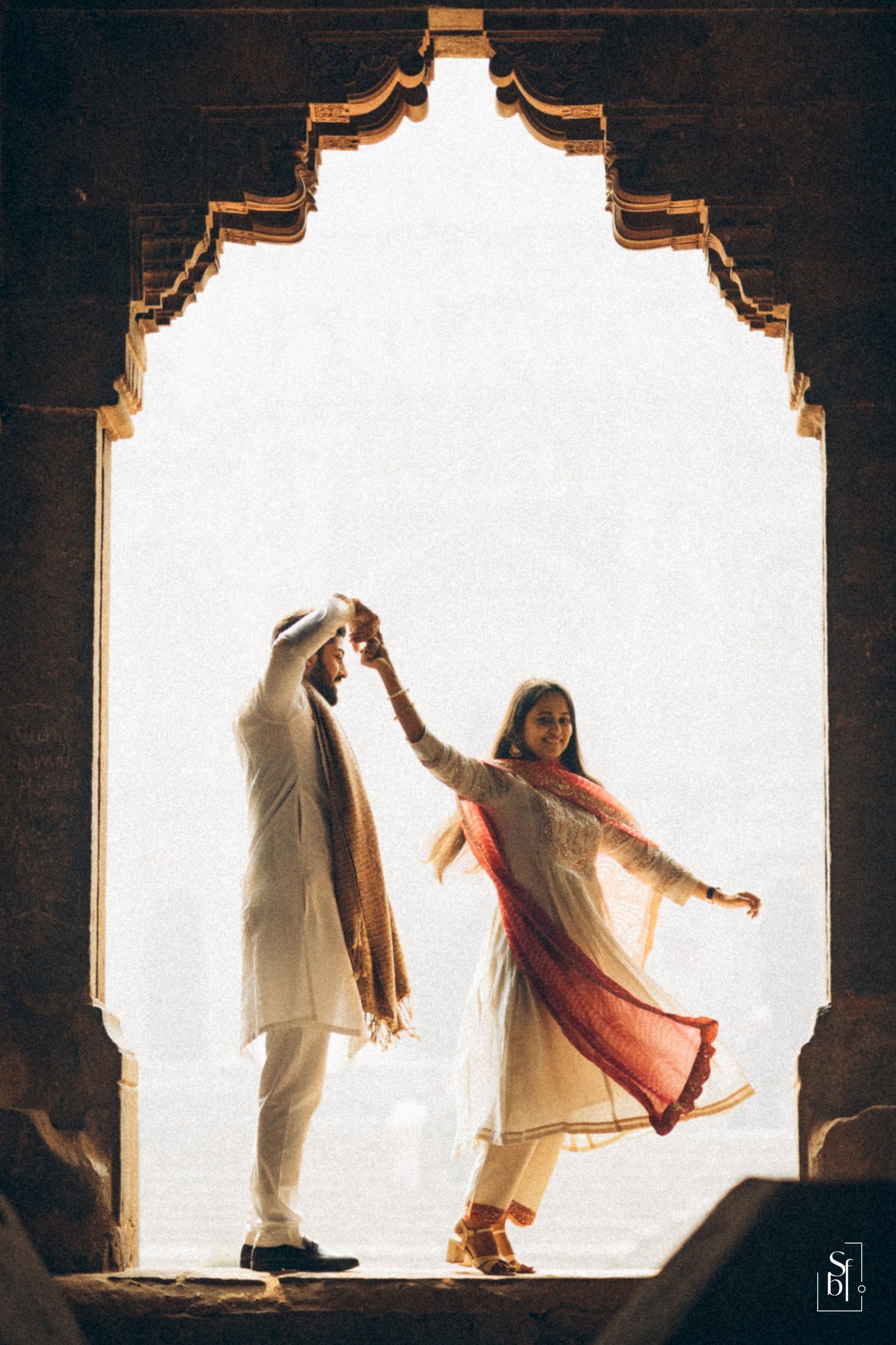 Couple twirling beneath a heritage stone archway during a pre-wedding shoot
